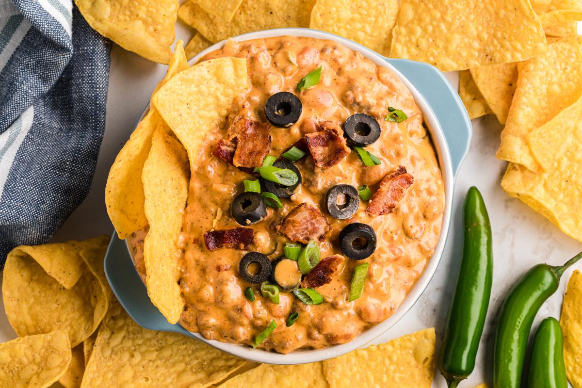 **Dip di Nachos Ricco Cotto Lentamente** 7 overhead shot of slow cooker loaded nacho dip in a bowl with chips in it.