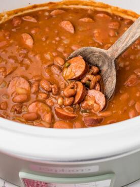 Fagioli e salsicce in una slow cooker con un cucchiaio di legno all'interno.