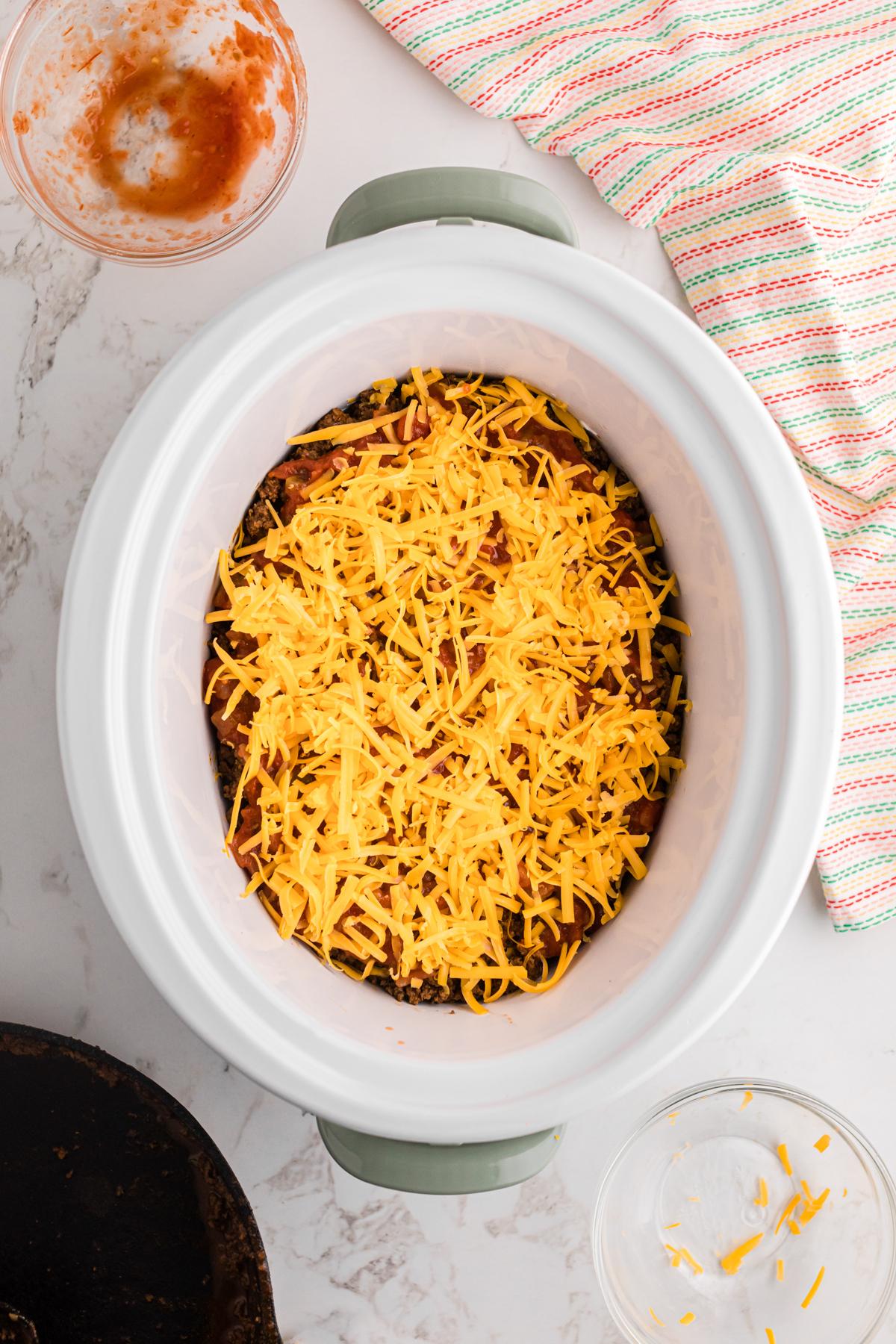 Salsa della Domenica Divertente 8 Formaggio cheddar cosparso sopra il composto di carne macinata in un slow cooker.