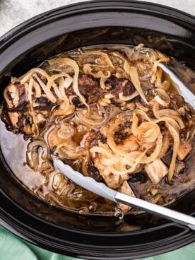 Costolette di birra e cipolla nella crockpot con pinze.