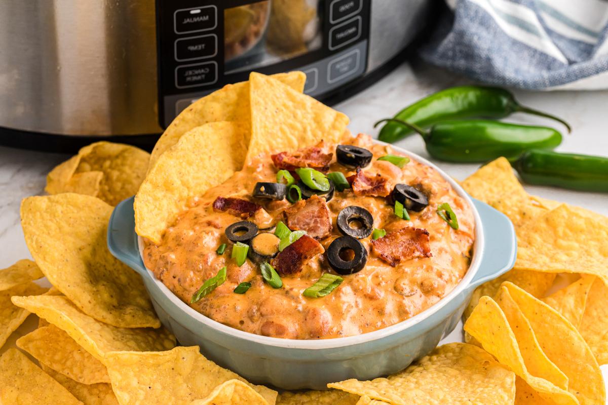 **Dip di Nachos Ricco Cotto Lentamente** 8 slow cooker loaded nacho dip in a white bowl with chips in and around it.
