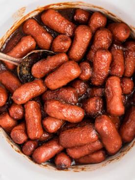 **Wurstel Piccoli al Burro di Mele in Slow Cooker** 8 Salsiccine mini al burro di mele nella slow cooker con un cucchiaio.