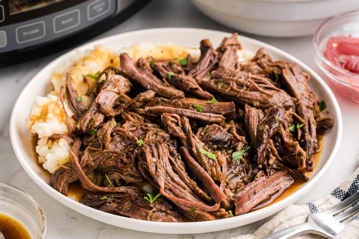 Un primo piano di una porzione di arrosto di manzo cotto in slow cooker su un piatto.
