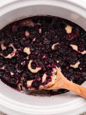 **Cobbler ai Mirtilli della Slow Cooker** 8 Cobbler di mirtilli al slow cooker con un cucchiaio di legno.