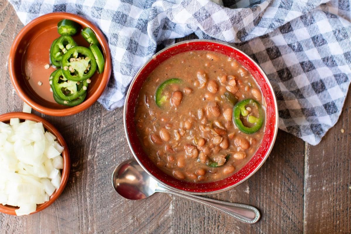 Fagioli Pinto Piccanti in Pentola a Cottura Lenta 8 Ciotola rossa con fagioli pinto. Jalapeños e cipolle sul lato.
