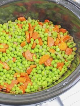 Piselli e carote in salsa burrosa e lucida all'interno della slow cooker, pronti per essere serviti