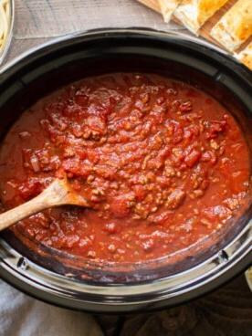 Sugo per Spaghetti a Cottura Lenta 9 Sugo cotto nella slow cooker con pane all'aglio e pasta sul lato.