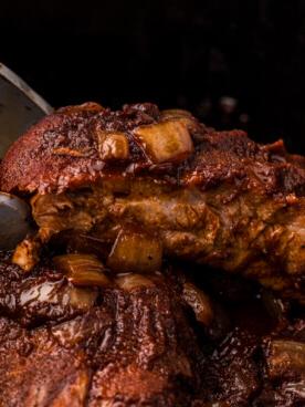 Costine di Maiale Stile Campagnolo a Cottura Lenta 9 primo piano delle pinze che prendono le costine di maiale stile country dalla slow cooker.
