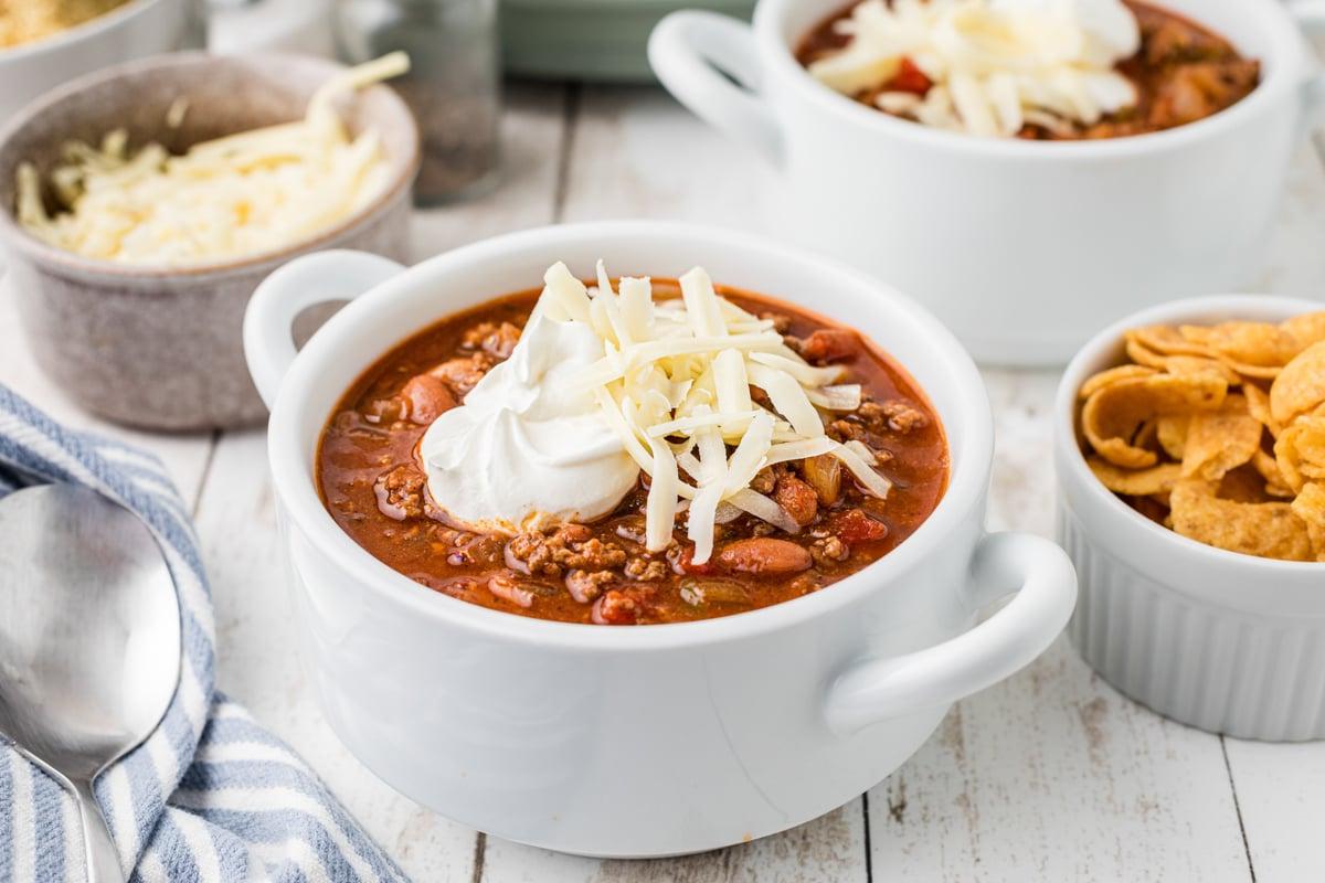 Miglior Chili per Slow Cooker 9 Chili in una ciotola bianca con panna acida e formaggio. Fritos sullo sfondo.