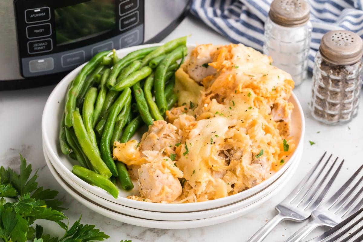 Casseruola di Pollo alla Reuben a Cottura Lenta 9 Porzione di sformato di pollo Reuben in slow cooker con fagiolini su un pila di piatti bianchi.