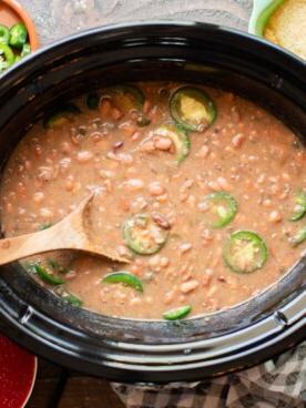 Fagioli Pinto Piccanti in Pentola a Cottura Lenta 9 Fagioli pinto nella slow cooker cotti con un mestolo di legno al loro interno.