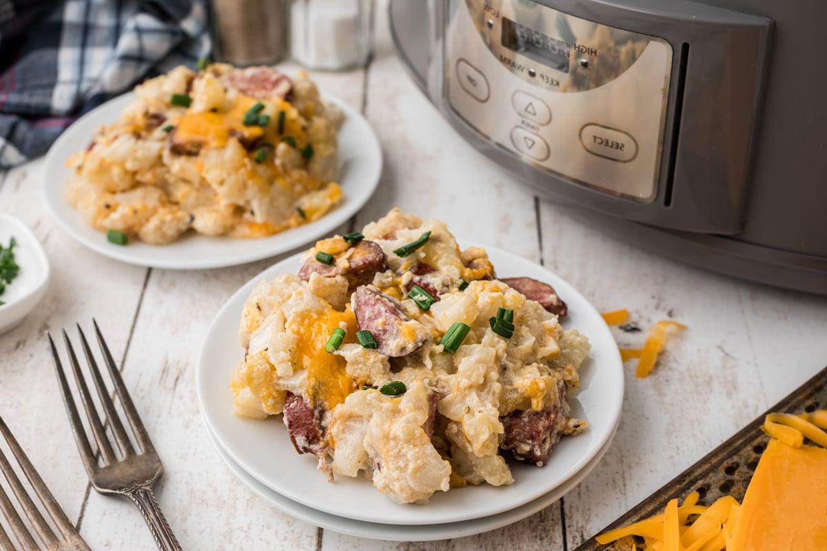 Sformato di Kielbasa e Hashbrowns in Cottura Lenta 9 Due piatti di casseruola di kielbasa e patate hashbrown al forno lento davanti a una slow cooker.