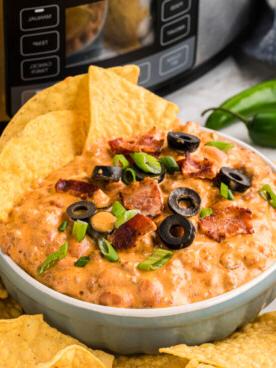 **Dip di Nachos Ricco Cotto Lentamente** 9 slow cooker loaded nacho dip in a white bowl with chips in and around it.