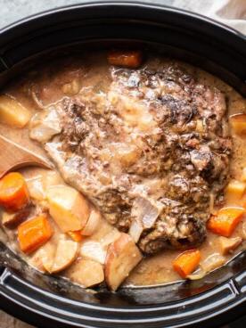 Brasato della Nonna per la Cena {con sugo che si forma da sé} 9 Arrosto di manzo con sugo, patate e cipolle in una pentola a cottura lenta con un cucchiaio di legno.