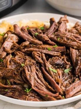 Un primo piano di una porzione di arrosto di manzo cotto in slow cooker su un piatto.