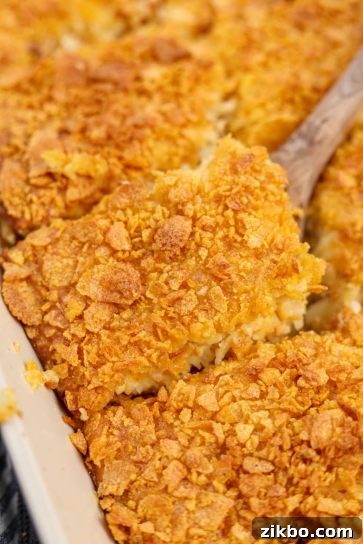 Ultimate Breakfast Hash Brown Bake 2 A wooden spatula serving up a square of breakfast casserole topped with crunchy cornflakes.