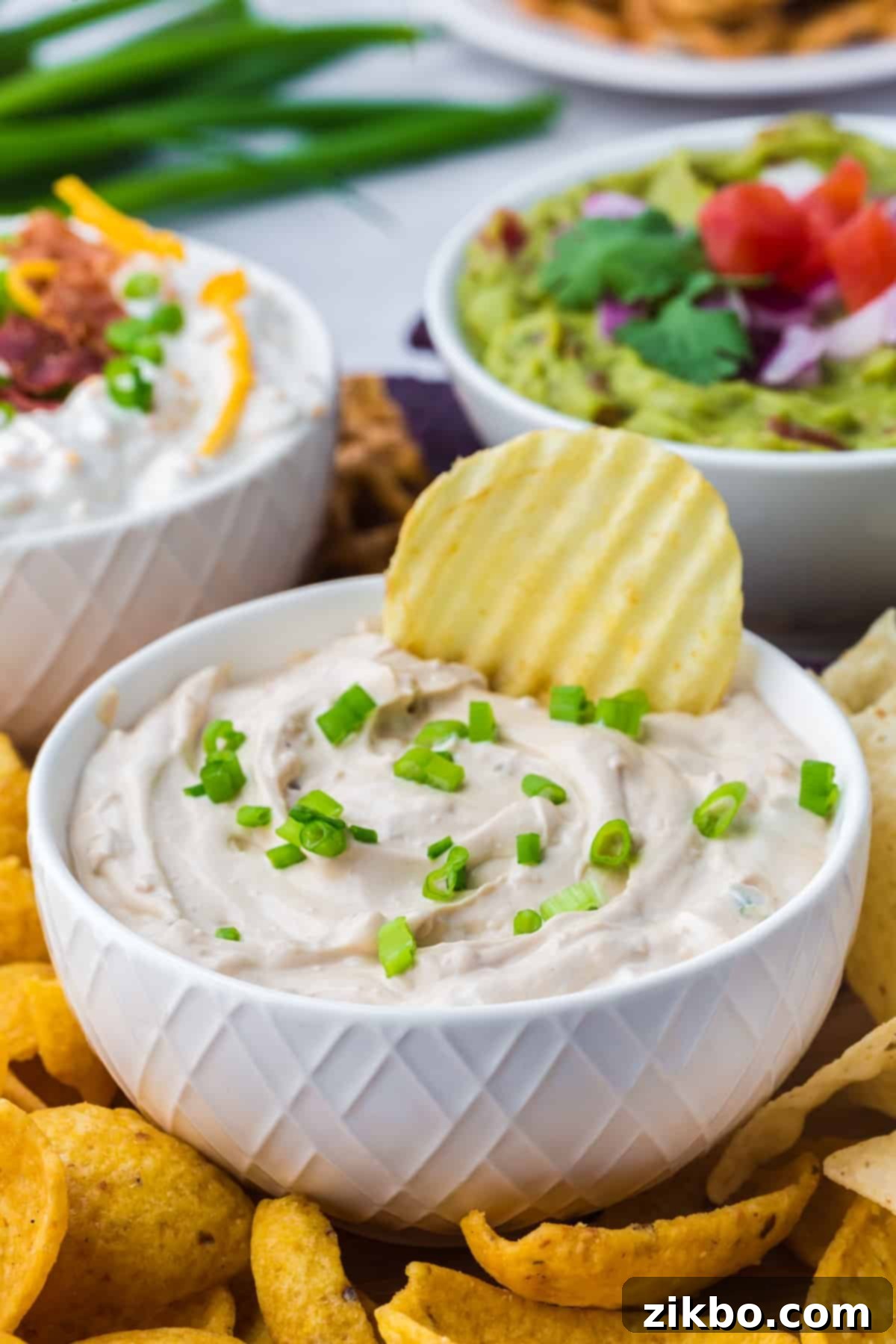 A chip being dipped into a bowl of rich, creamy homemade French Onion Dip, garnished with fresh green onions.