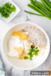 A white bowl filled with sour cream, onion mix, garlic, green onions, etc.
