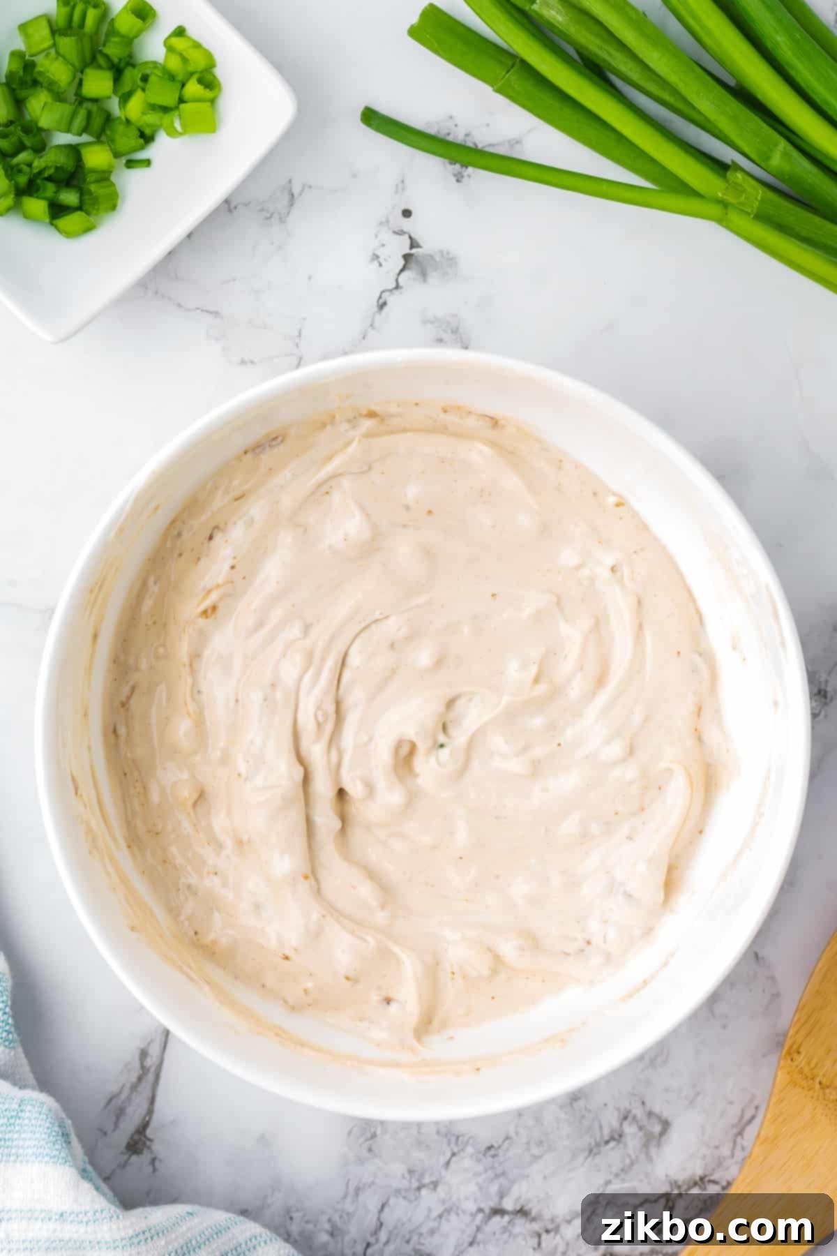 A bowl of creamy French onion dip, freshly mixed, with green onions scattered around the edges as a potential garnish.
