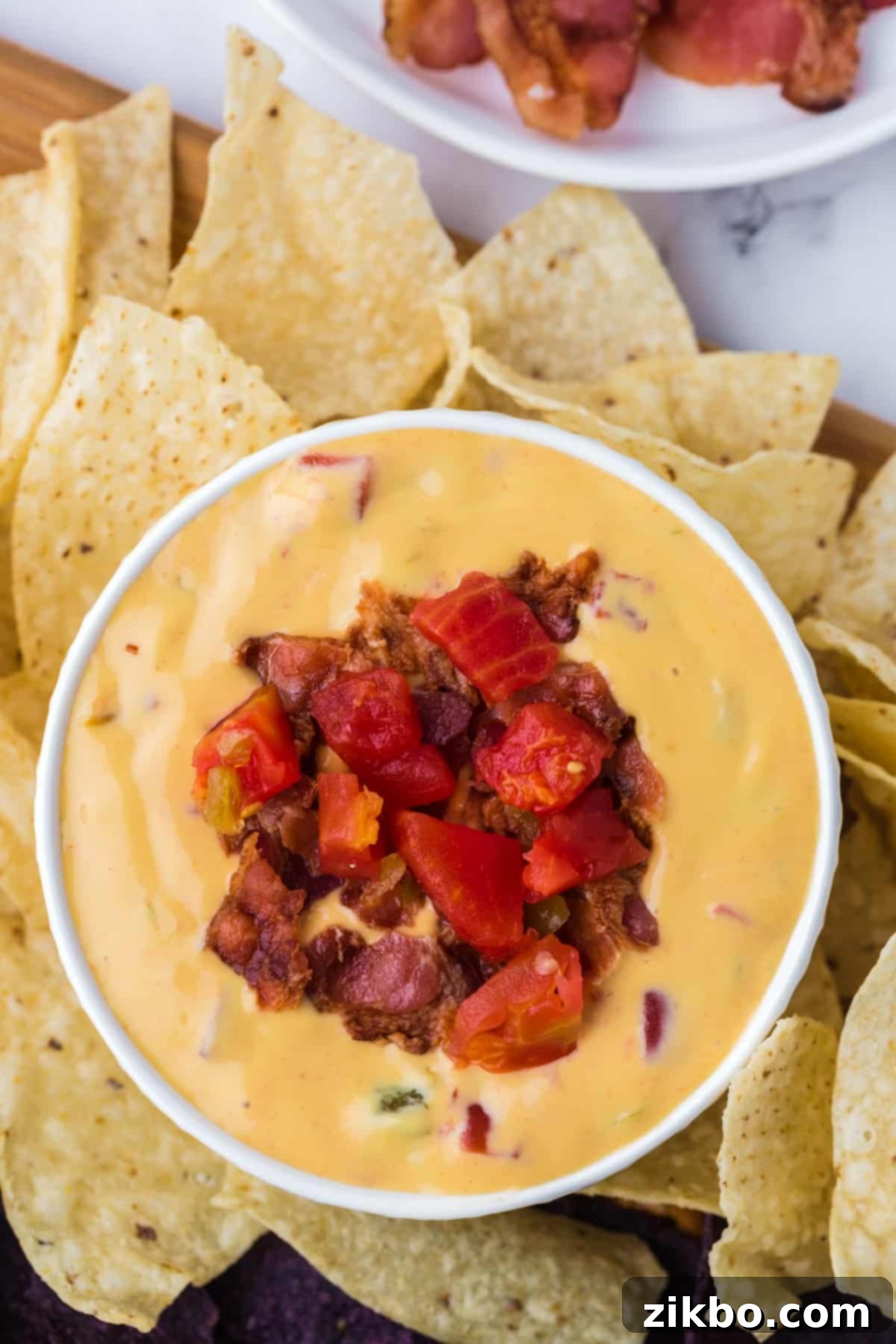 A small bowl of nacho cheese dip garnished with bacon and tomato, served with tortilla chips.