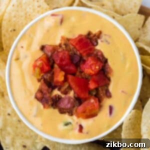 A white bowl filled with nacho cheese dip that's been garnished with bacon bits and tomato. Served with tortilla chips around the outside.