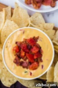 A small bowl of nacho cheese dip garnished with bacon and tomato.