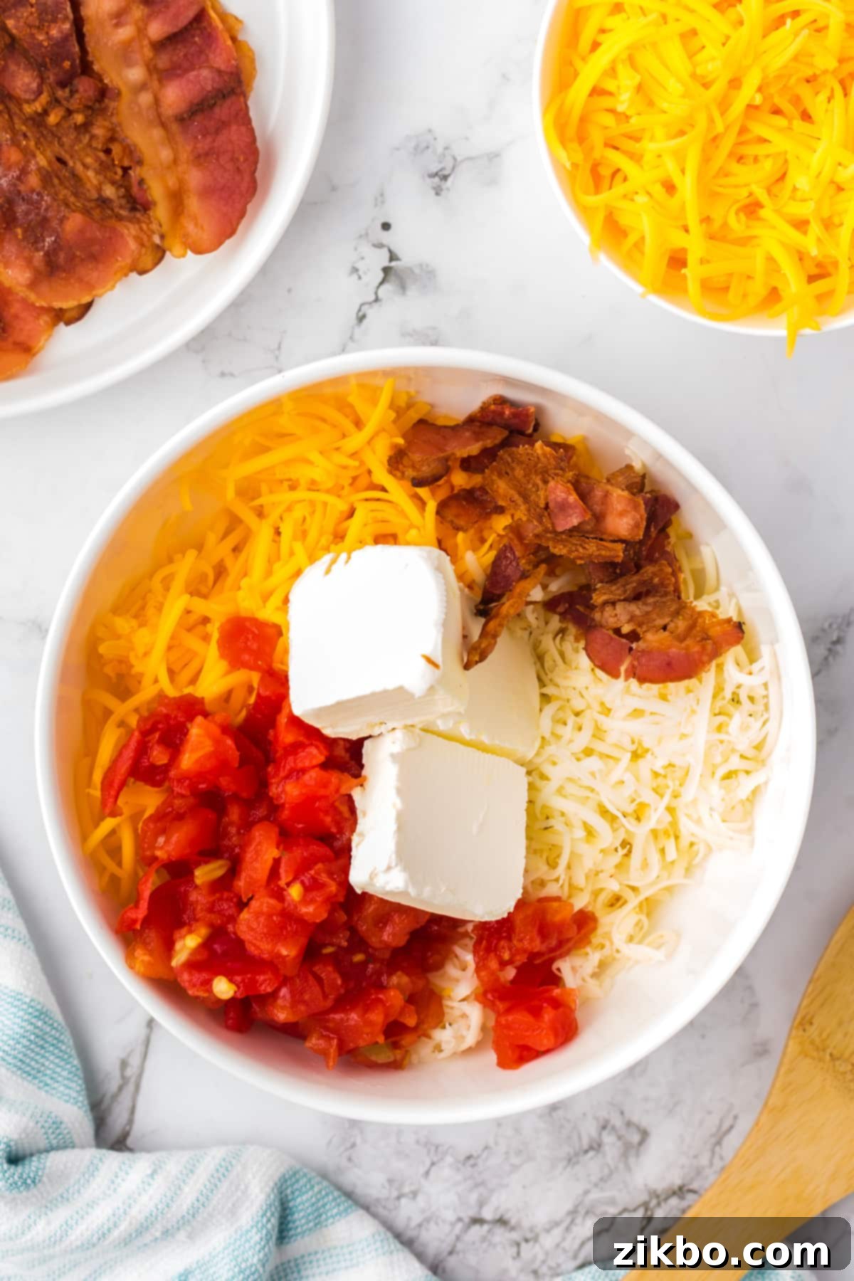 A large bowl filled with shredded cheeses, cream cheese, crumbled bacon, and rotel tomatoes, ready to be melted.
