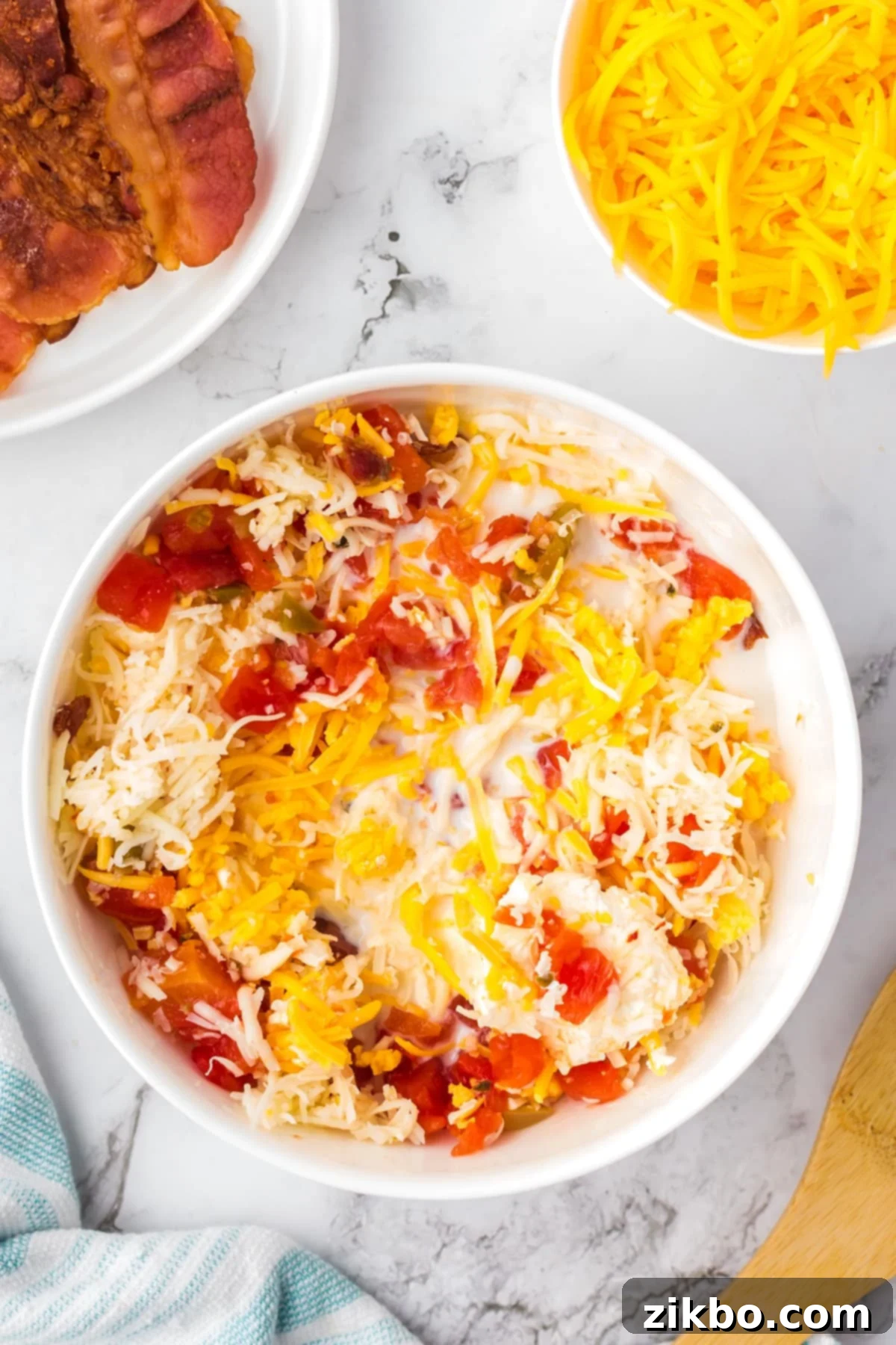 A large bowl with cheese and cream cheese being mixed together with bacon and rotel tomatoes, starting to melt.