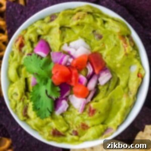 Robust Chunky Guacamole 8 A bowl of guacamole topped with red onion, tomato, and cilantro.