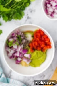 A bowl of mashed avocado topped with red onion, tomato, garlic, pepper, salt, and cilantro.