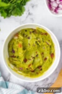 A bowl of guacamole featuring chunks of tomato.