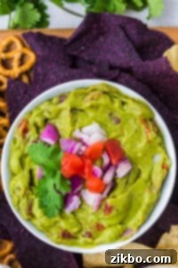 A bowl of guacamole topped with chopped tomato and red onion.