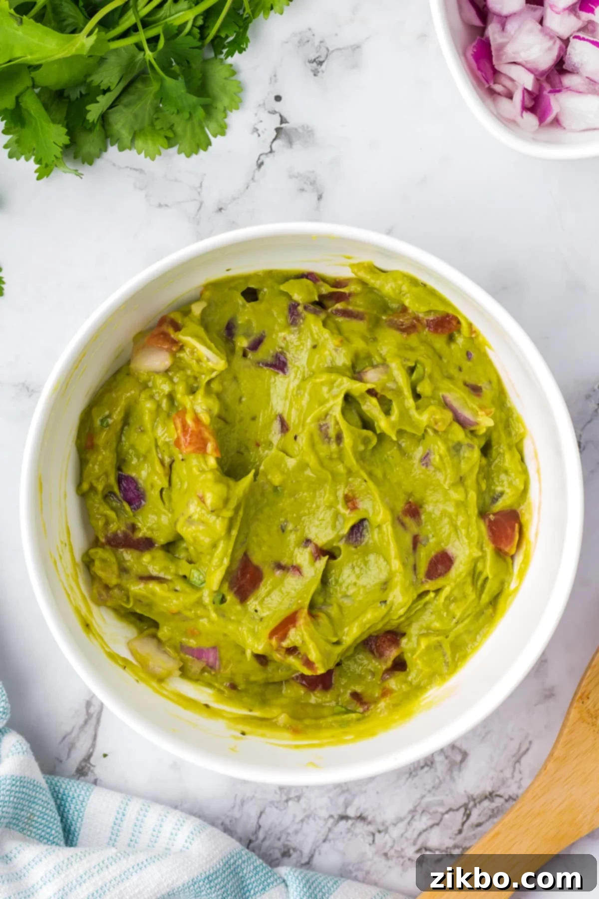 Robust Chunky Guacamole 5 A bowl of chunky guacamole featuring visible chunks of tomato and onion, stirred and ready to serve.