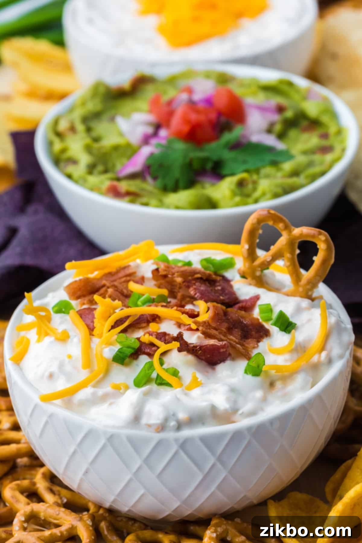 Ultimate Loaded Baked Potato Dip 2 A bowl of baked potato dip with a pretzel dipped on the side, showing its creamy texture and delicious toppings.