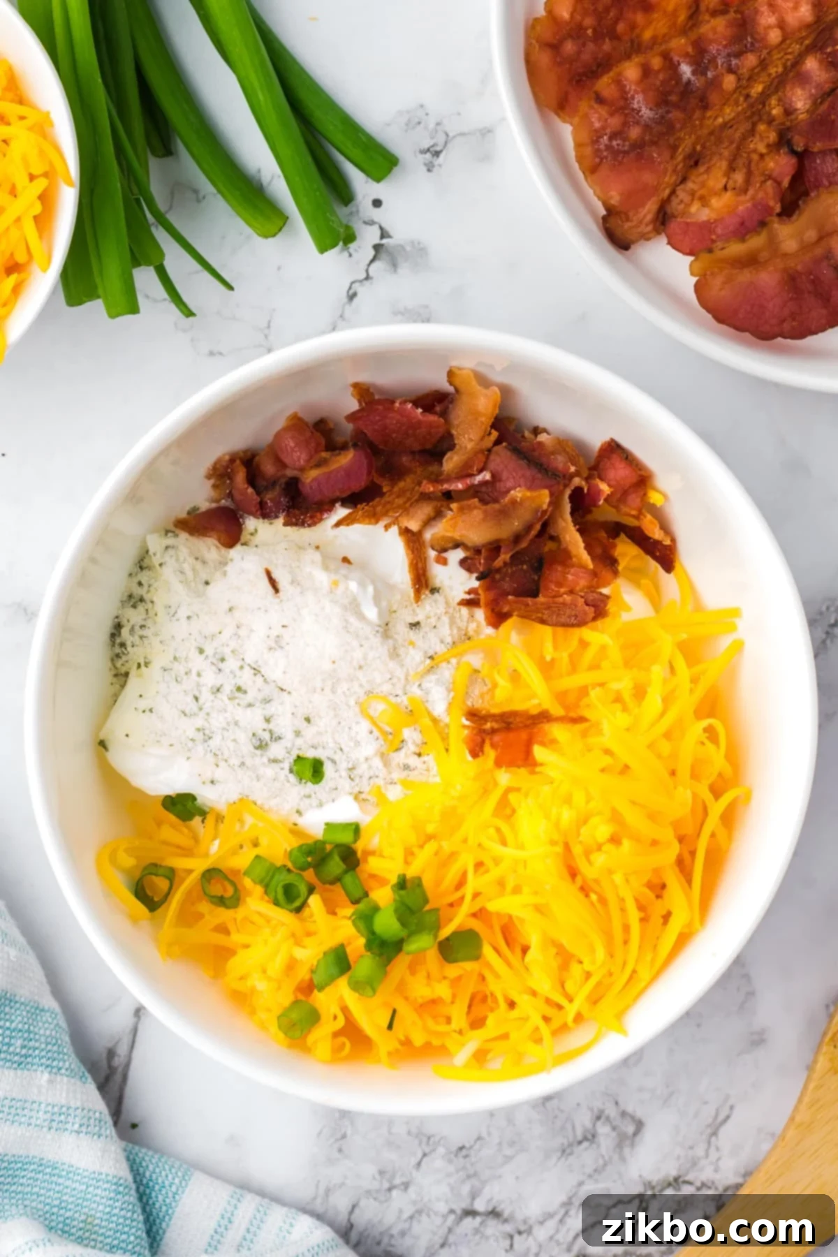 Ultimate Loaded Baked Potato Dip 4 A white bowl featuring shredded cheese, bacon, ranch seasoning, and green onions, waiting to be mixed with sour cream.