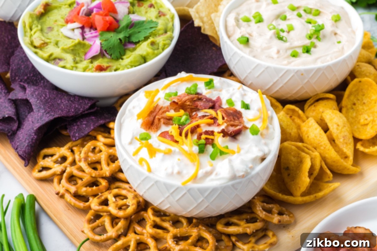 Ultimate Loaded Baked Potato Dip 8 Three bowls of various creamy dips, including the loaded baked potato dip, surrounded with colorful blue corn tortilla chips, classic corn chips, and crunchy pretzels, creating an inviting appetizer spread.