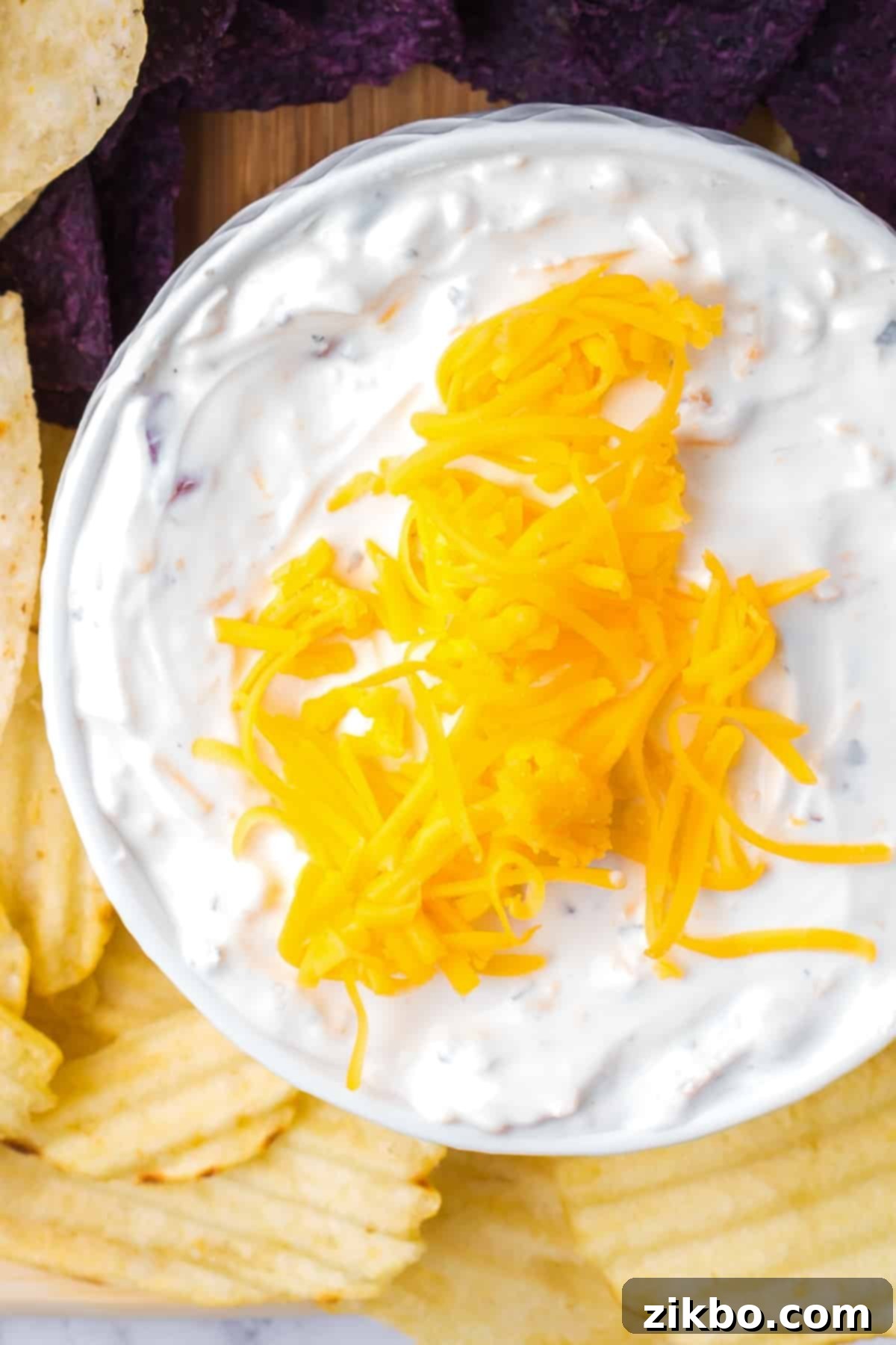 A bowl of creamy dip topped generously with shredded cheddar cheese, ready to be served.