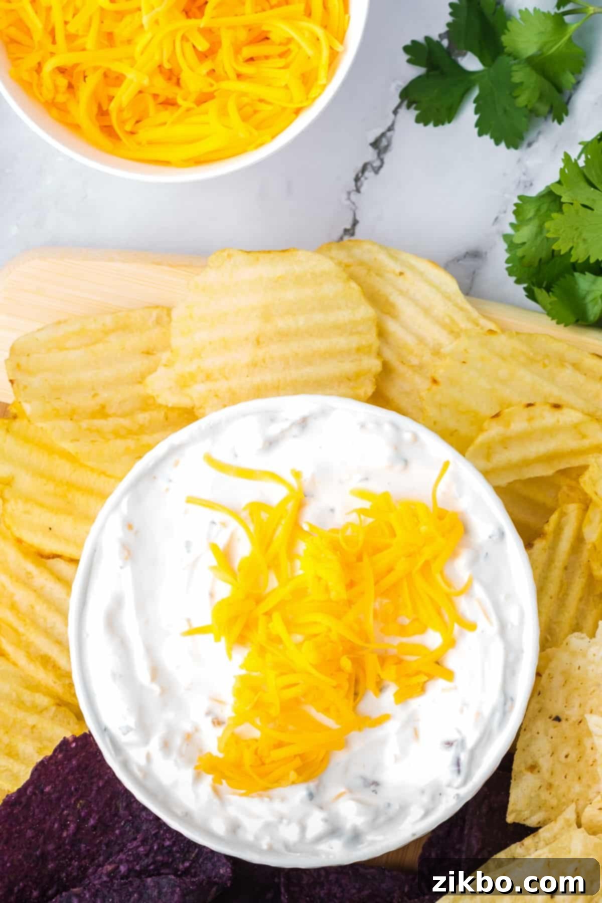 A small bowl of creamy beer cheese dip topped with shredded cheddar cheese, with ridged potato chips arranged artfully on the side.