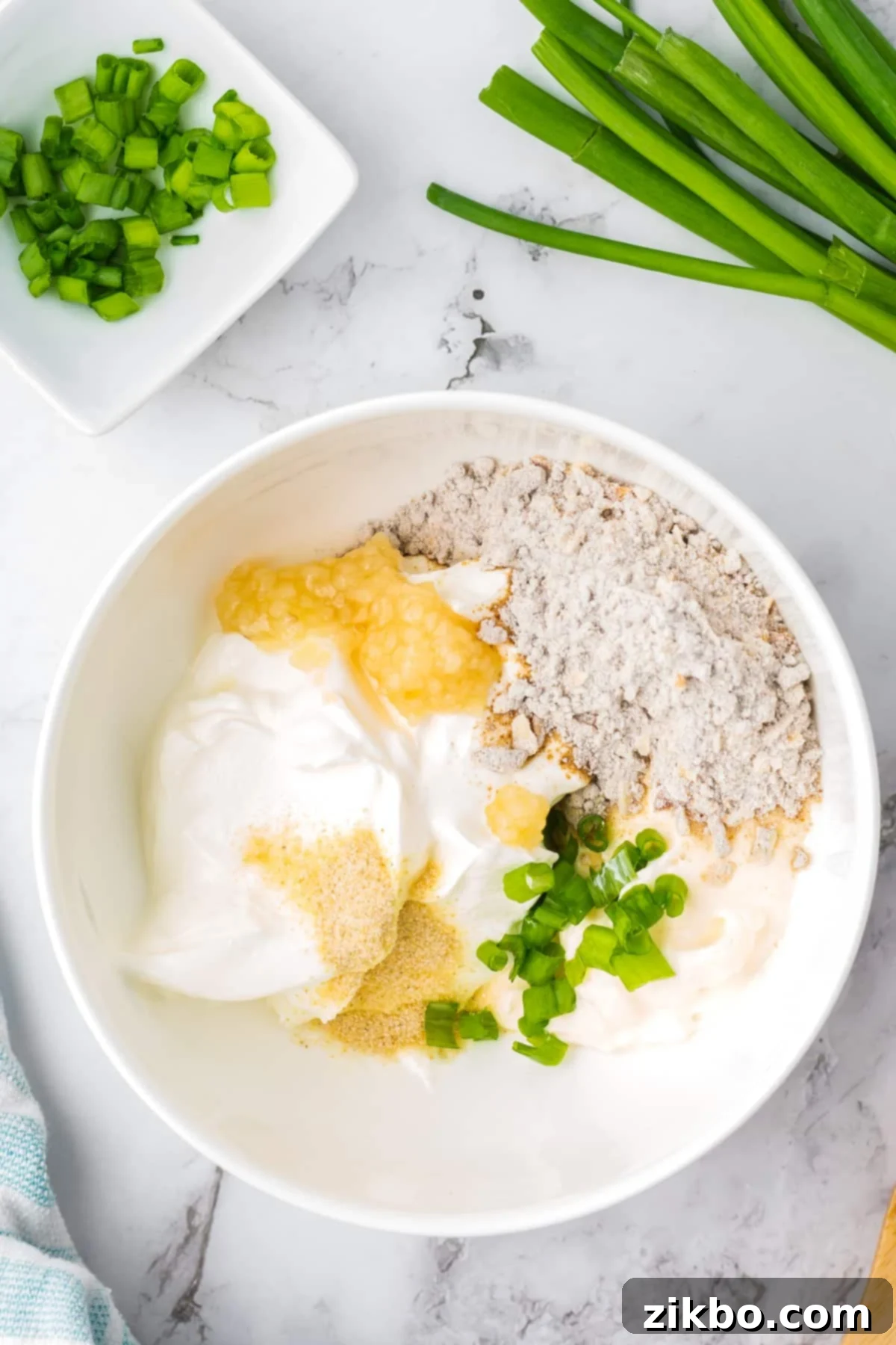 A white bowl filled with sour cream, onion mix, garlic, green onions, etc.