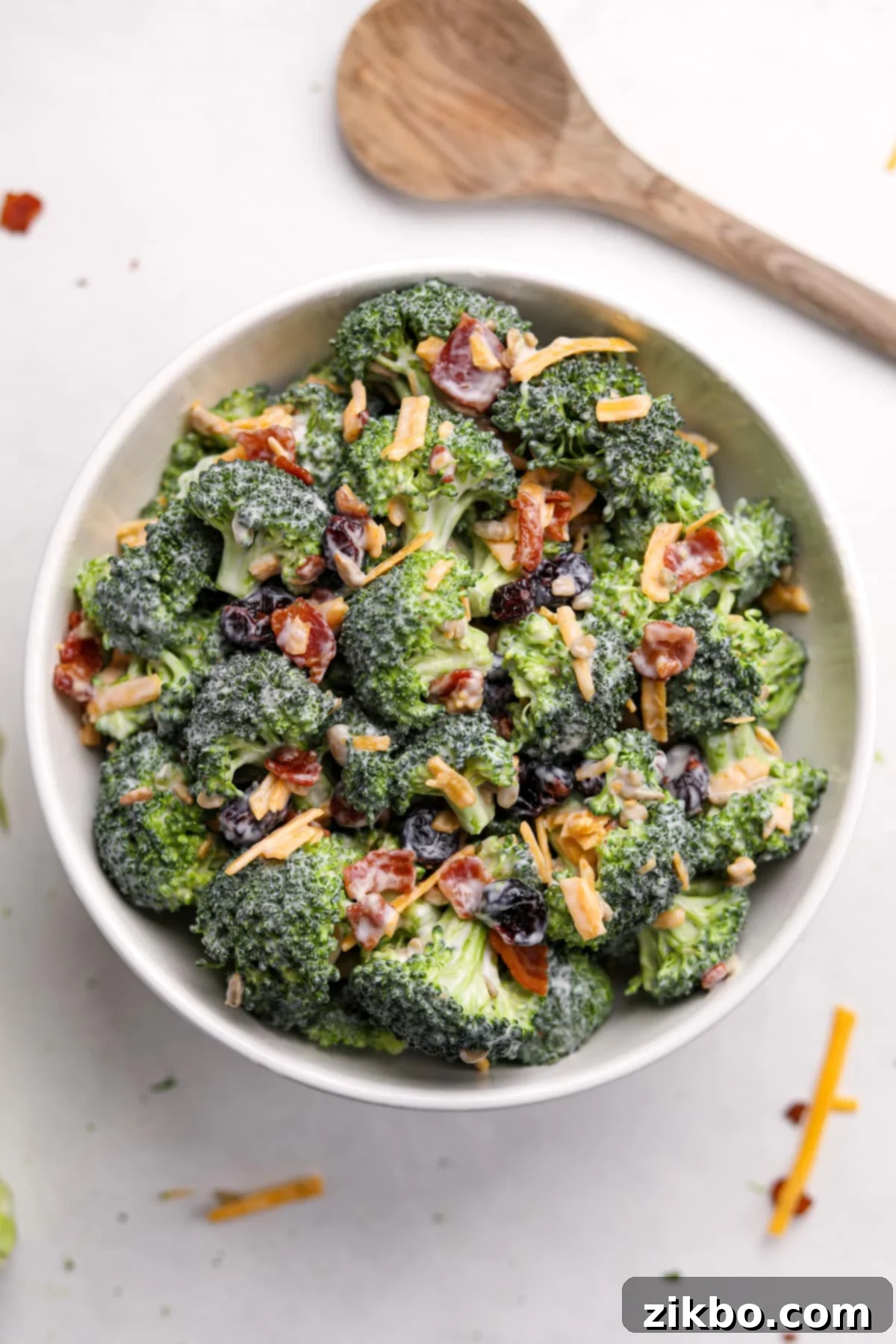 Crunchy Broccoli Delight 11 A white bowl filled with finished creamy broccoli salad, garnished with extra bacon and cheddar cheese for serving.