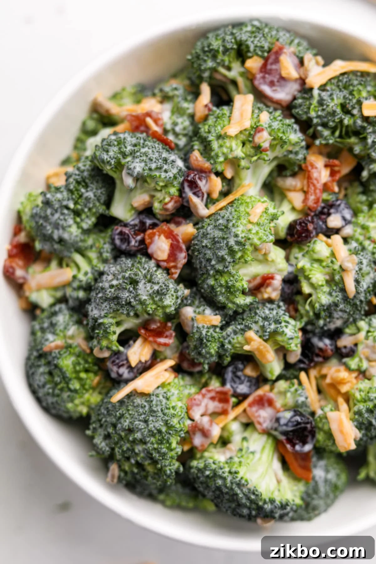 Crunchy Broccoli Delight 12 A close up of a bowl of creamy broccoli salad, beautifully featuring bacon crumbles and sharp cheddar cheese shreds on top.