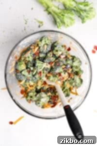 A bowl of creamy broccoli salad that's been mixed with a silicone spatula to combine all ingredients evenly.