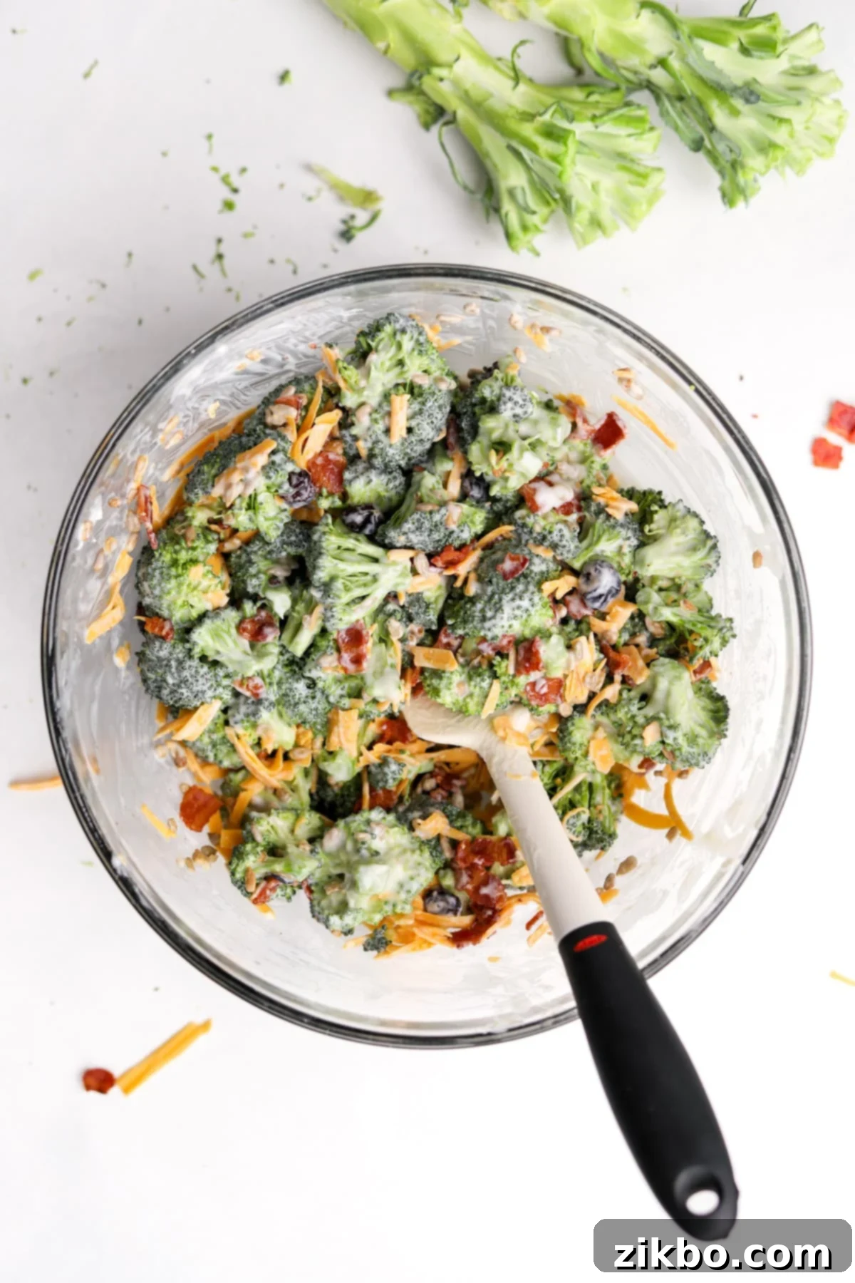 Crunchy Broccoli Delight 10 A bowl of creamy broccoli salad that's been thoroughly mixed with a silicone spatula, showing even distribution of ingredients.