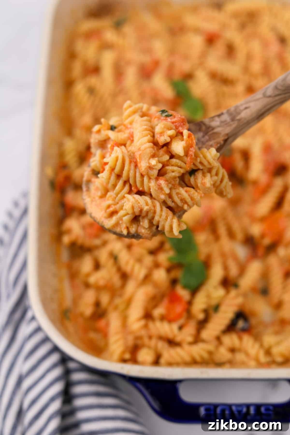 Tangy Goat Cheese Pasta Bake 11 A serving of creamy baked goat cheese pasta being scooped from a casserole dish, garnished with fresh basil.
