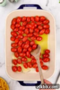 Stirring olive oil and grape tomatoes together in a baking dish.