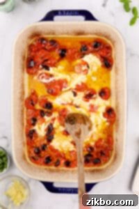 Stirring goat cheese into cherry tomatoes in a baking dish.