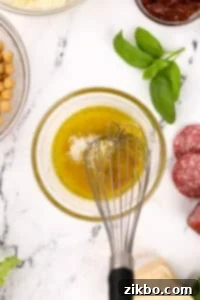 Whisking together a dressing that includes olive oil and Parmesan cheese until fully emulsified.
