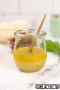 A small jar of homemade vinaigrette, Leon dressing, with a gold spoon inside, ready for serving.