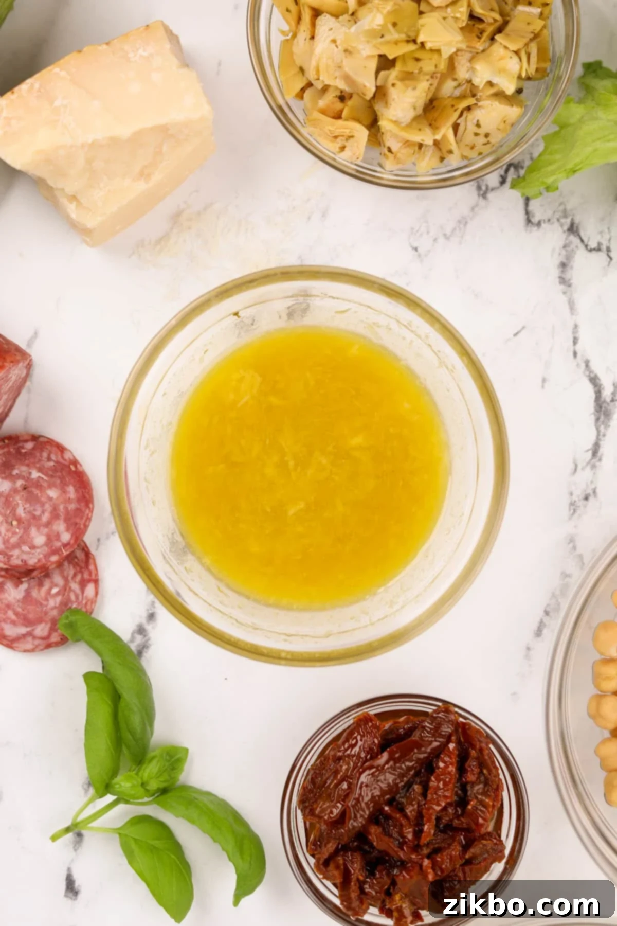Leon's Artisan Blend 6 A small bowl of bright, golden vinaigrette surrounded by fresh antipasto ingredients like olives, cheese, and salami, ready to be served.