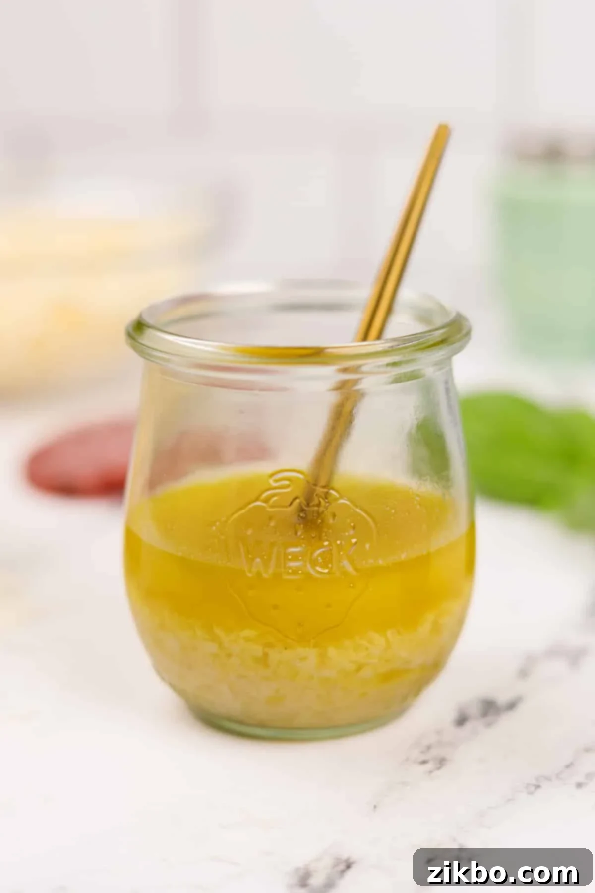 Leon's Artisan Blend 7 A clear glass jar of homemade Leon salad dressing with a small gold spoon inside, showcasing its vibrant color and texture.